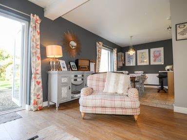 A living room with a plaid armchair a sideboard with a lamp and mirror and a dining area with framed pictures at The Croft in Newport Pembrokeshire