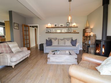 A living room with a plaid armchair a gray sofa wooden shelves with pictures a wood burning stove and a wooden crate coffee table at The Croft in Newport Pembrokeshire