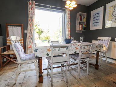 A dining room with a table covered by a starfish patterned tablecloth and wooden chairs with cushions at The Croft in Newport Pembrokeshire