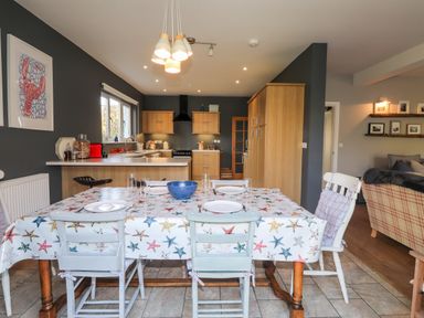 A dining table with starfish tablecloth and plates set in a kitchen with wooden cabinets and chairs at The Croft in Newport Pembrokeshire