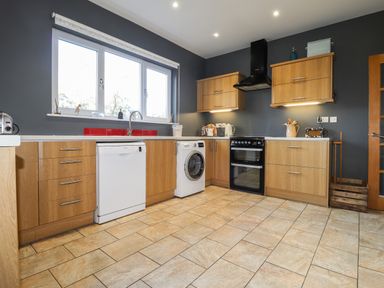 A kitchen with wooden cabinets a dishwasher washing machine oven and tiled floor at The Croft in Newport Pembrokeshire