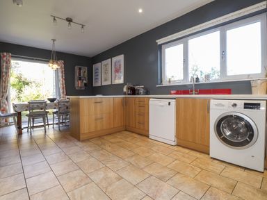 A kitchen with wooden cabinets a washing machine dishwasher and a dining table near a window at The Croft in Newport Pembrokeshire
