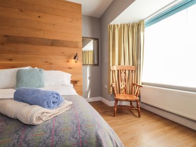 A bedroom with a bed with folded towels and a wooden chair by a window with curtains at The Croft in Newport Pembrokeshire