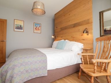 A bedroom with a bed with white and gray bedding wooden chair and wooden wall paneling at The Croft in Newport Pembrokeshire
