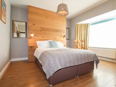 A bedroom with a double bed wooden headboard a wooden chair a large window and wooden floor at The Croft in Newport Pembrokeshire