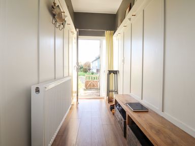 A narrow hallway with wooden floor a wooden bench with storage baskets a radiator and an open door leading outside at The Croft in Newport Pembrokeshire
