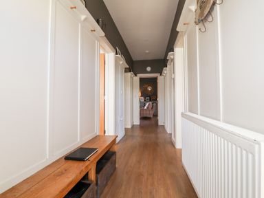 A hallway with wooden floor a wooden bench and white paneled walls leading to a room with a chair and decorative mirror at The Croft in Newport Pembrokeshire