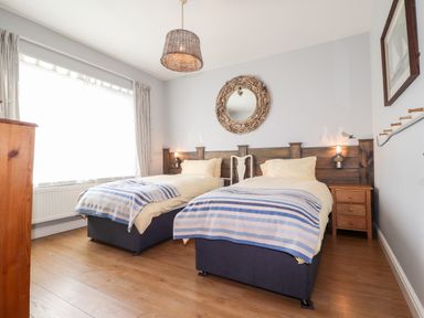 A bedroom with two single beds blue striped blankets wooden nightstand and circular mirror at The Croft in Newport Pembrokeshire