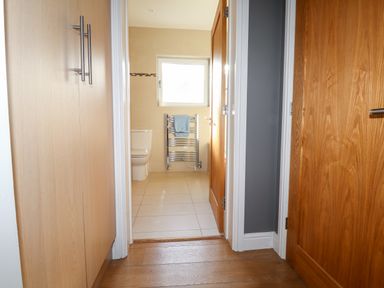 A hallway with wooden floorboards leading to a bathroom with a tiled floor a toilet a towel rack and a window at The Croft in Newport Pembrokeshire