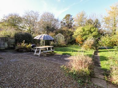 A garden with a picnic table and umbrella a barbecue grill gravel area and grass at The Croft in Newport Pembrokeshire
