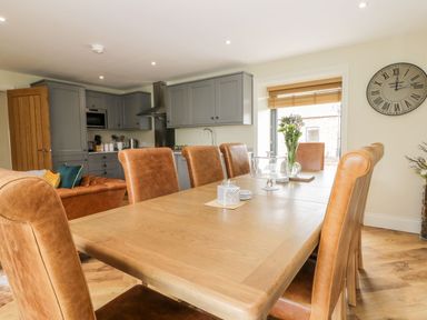 A dining area with a wooden table and leather chairs next to a kitchen with gray cabinets and a clock on the wall at Partridge Place Burton Pidsea