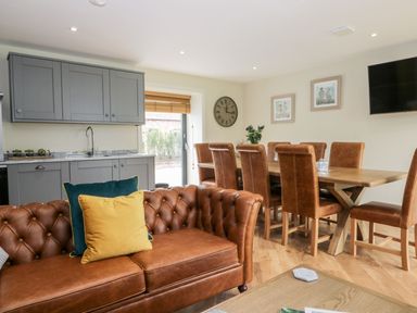 A dining area with brown leather chairs around a wooden table and a leather sofa with cushions near a kitchen with grey cabinets at Partridge Place Burton Pidsea