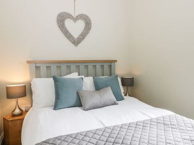 A bedroom with a bed with blue and gray pillows two bedside lamps and a heart shaped wall decoration at Partridge Place in Burton Pidsea