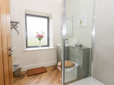 A bathroom with a toilet a shower a window with flowers a waste bin and wood flooring at Partridge Place in Burton Pidsea