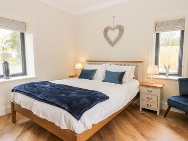 A bedroom with a bed with white bedding and blue pillows between two windows with bedside tables and lamps at Partridge Place in Burton Pidsea