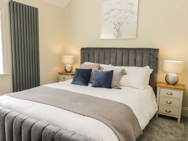 A bedroom with a gray upholstered bed two bedside tables with lamps and a painting above the bed at Partridge Place in Burton Pidsea
