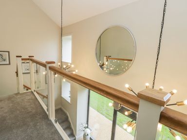 An upper floor hallway with glass and wood railing a round wall mirror and hanging lights at Partridge Place in Burton Pidsea