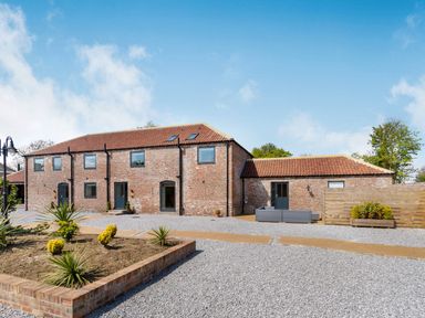A brick building with multiple windows and doors surrounded by gravel and a small garden area at Partridge Place in Burton Pidsea