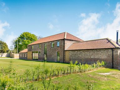 An exterior view of a brick house with a tiled roof and surrounding grass and small plants at Partridge Place in Burton Pidsea