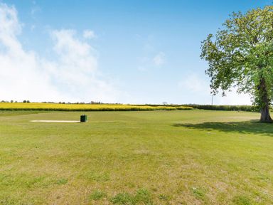 A grassy field with a tree on the right and a small green bin on a concrete slab under a blue sky at Partridge Place in Burton Pidsea