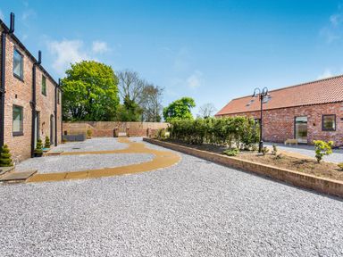 An outdoor area with gravel, pathways, brick buildings, plants, and trees at Partridge Place in Burton Pidsea