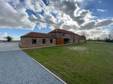A brick building with a tiled roof next to a gravel path and grass field at Partridge Place in Burton Pidsea