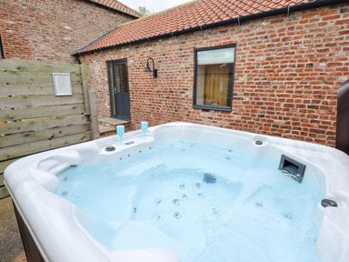 An outdoor hot tub with two blue glasses near a brick house with a black door and window at Partridge Place in Burton Pidsea