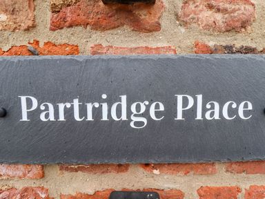 A dark stone sign with white text reading Partridge Place mounted on a red brick wall at Partridge Place Burton Pidsea