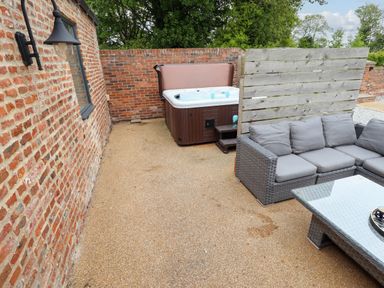 An outdoor patio with a hot tub a sectional sofa a glass coffee table and brick walls at Partridge Place in Burton Pidsea