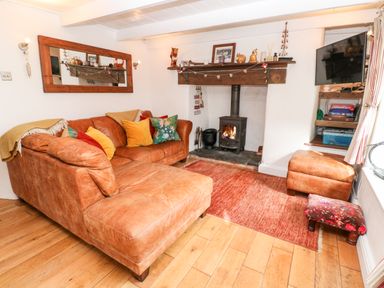 A living room with a leather sectional sofa and a wood burning stove at Honeysuckle Cottage in St Agnes