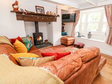 A living room with a brown leather sofa colorful cushions a wood burning stove and a wall mounted television at Honeysuckle Cottage in St Agnes