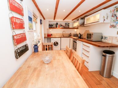 A kitchen with wooden table and chairs washing machine oven microwave and wall shelves at Honeysuckle Cottage in St Agnes