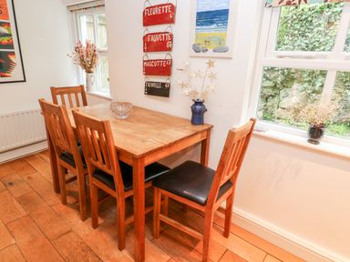 A dining area with a wooden table four wooden chairs and decorative items on windowsills and walls at Honeysuckle Cottage in St Agnes