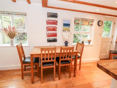 A dining area with a wooden table and four chairs plants on window sills and wall art at Honeysuckle Cottage in St Agnes