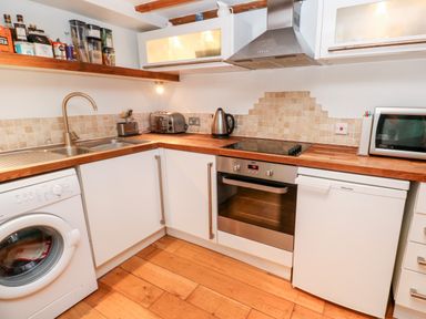 A kitchen with a washing machine sink toaster kettle oven fridge and microwave at Honeysuckle Cottage in St Agnes