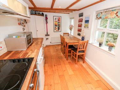 A kitchen with wooden countertops and floor a dining table with four chairs and windows with floral blinds at Honeysuckle Cottage in St Agnes