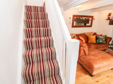 Striped carpeted stairs next to a brown leather sofa with cushions in a living room at Honeysuckle Cottage in St Agnes