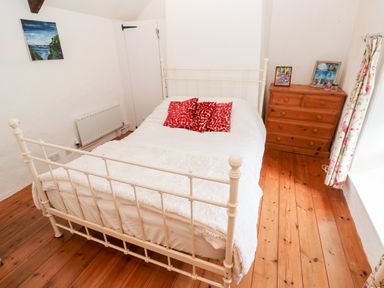 A bedroom with a white metal bed frame a wooden chest of drawers and a small painting on the wall at Honeysuckle Cottage in St Agnes