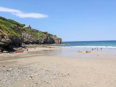 A sandy beach with people and kayaks near cliffs and ocean at Honeysuckle Cottage in St Agnes