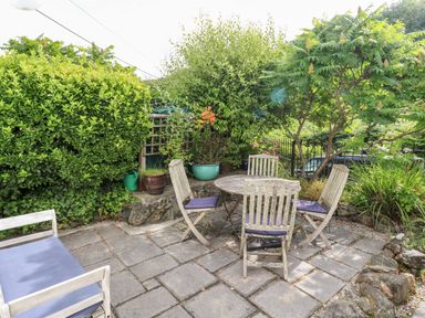 An outdoor patio with a round table and four chairs surrounded by plants and bushes at Honeysuckle Cottage in St Agnes