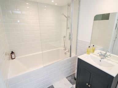 A bathroom with a bathtub shower combination and a sink with a mirror at Honeysuckle Cottage in St Agnes