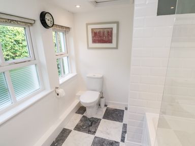 A bathroom with a toilet a clock on the wall two windows and a bathtub at Honeysuckle Cottage in St Agnes