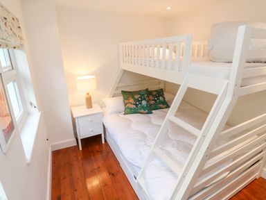 A bedroom with a white bunk bed, a small white bedside table with a lamp, and wooden floorboards at Honeysuckle Cottage in St Agnes