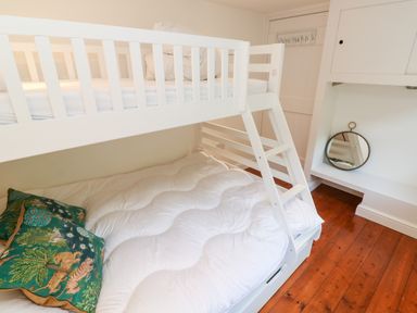 A bedroom with white bunk beds wooden floor and decorative pillows at Honeysuckle Cottage in St Agnes