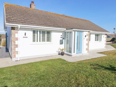 A single story house with a blue door and white walls with windows and a lawn at Palm View in Holywell Bay