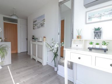 A hallway with white furniture plants and a large mirror at Palm View in Holywell Bay