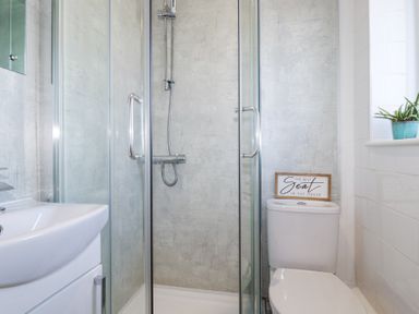 A bathroom with a shower enclosure a toilet with a sign and a sink with a mirror at Palm View in Holywell Bay