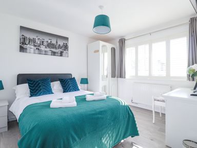 A bedroom with a double bed teal bedding and pillows white wardrobe and desk at Palm View in Holywell Bay
