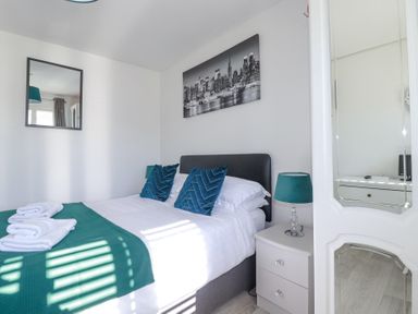 A bedroom with a bed teal pillows teal lamp and a mirror at Palm View in Holywell Bay