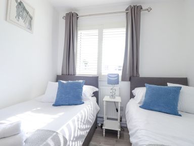 A bedroom with two single beds a bedside table and window with curtains at Palm View in Holywell Bay